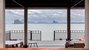 A terrace with tables and chairs overlooking a calm body of water and distant islands.
