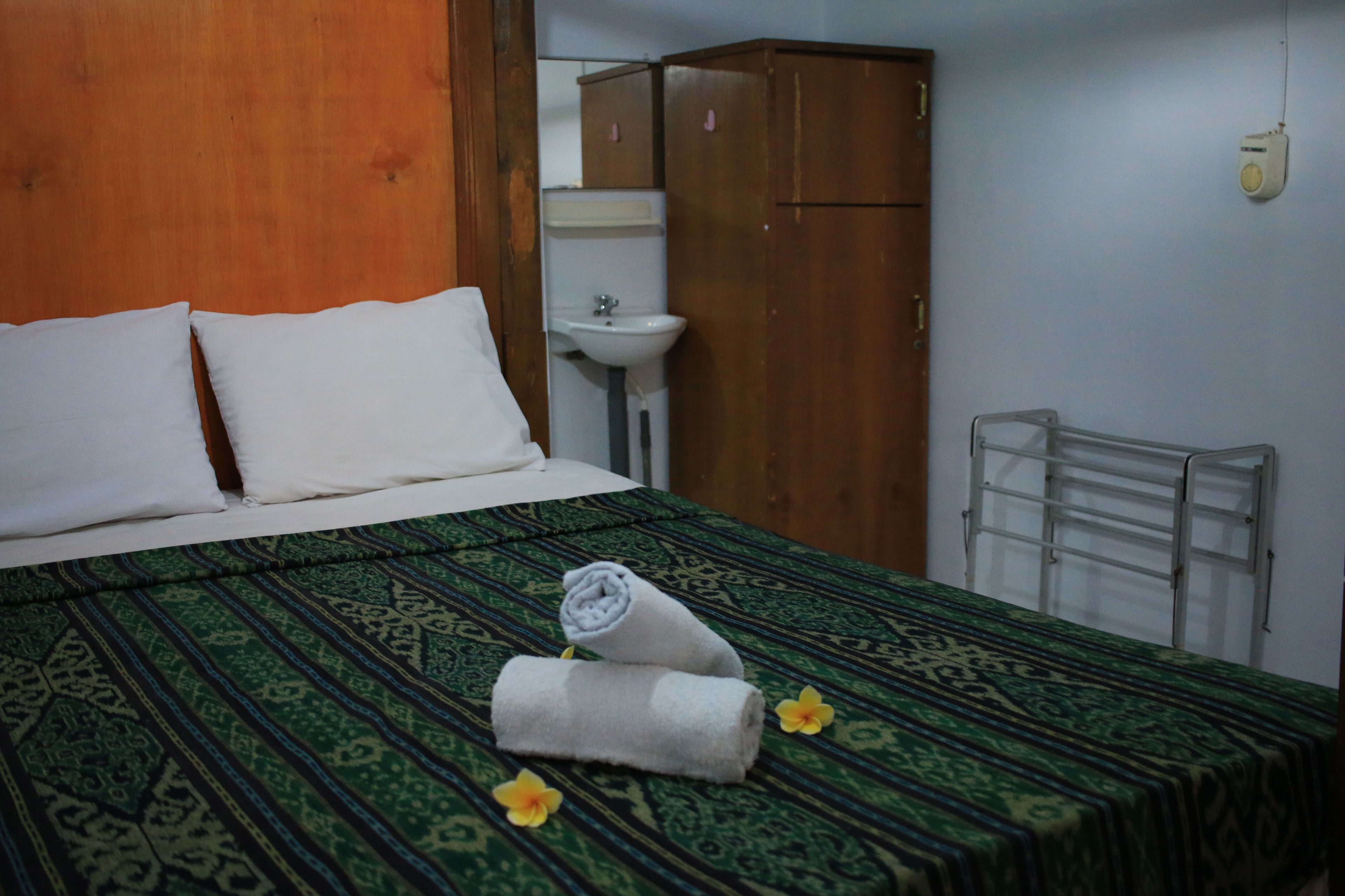 A neatly made bed with a patterned bedspread, a rolled towel, and a flower on the bed.