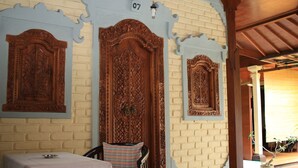 A room with a brick wall, a wooden door with intricate carvings, and a table with a white tablecloth. - Simon Homestay (Denpasar)