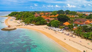 A beach resort with a sandy shoreline, clear turquoise waters, and a cluster of buildings with red roofs. - Simon Homestay (Denpasar)