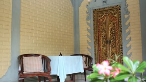 A dining area with a brick wall, a table with a tablecloth, wooden chairs, and a decorative door. - Simon Homestay (Denpasar)