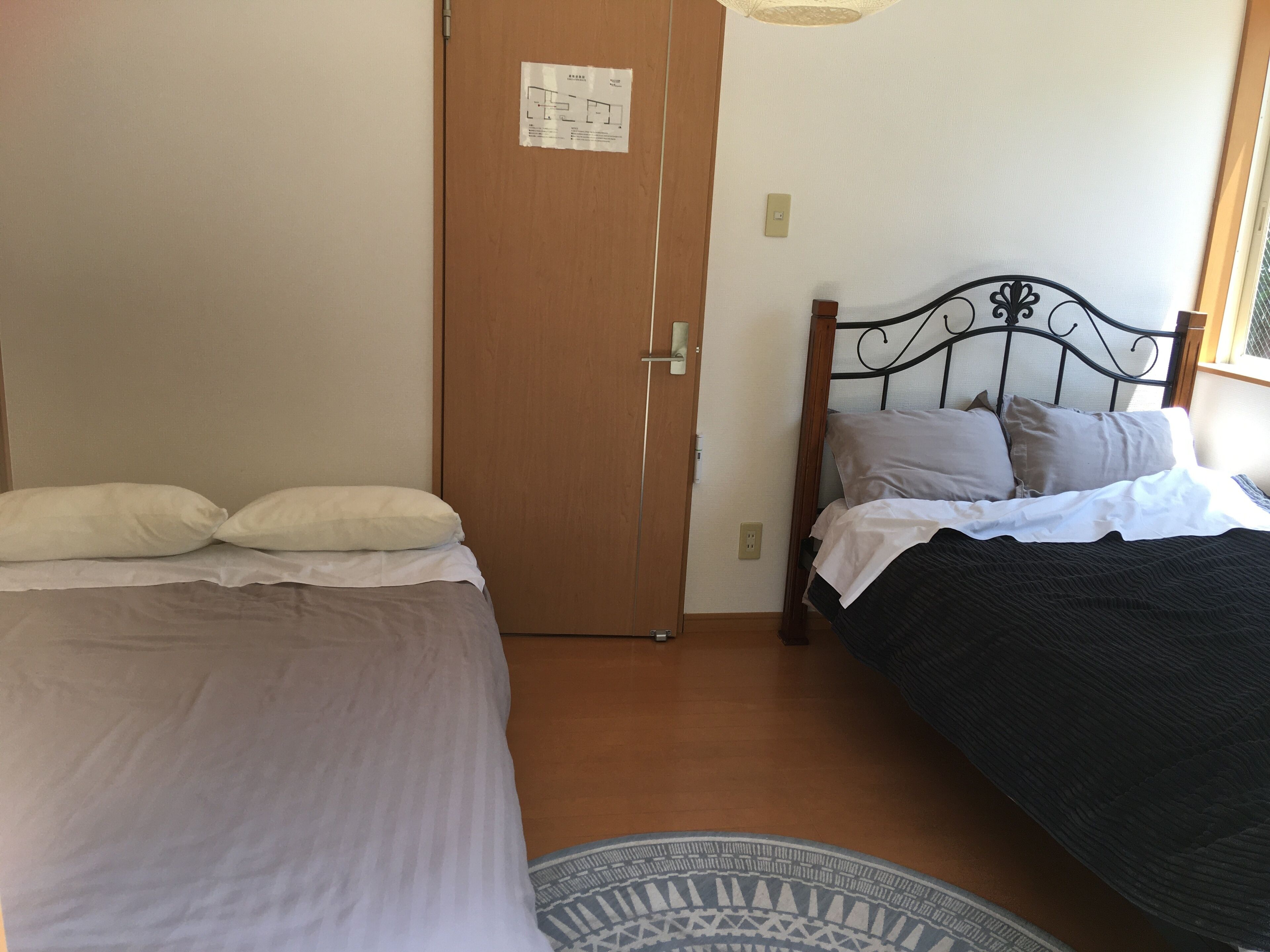 A bedroom with two beds, a wooden door, and a patterned rug.