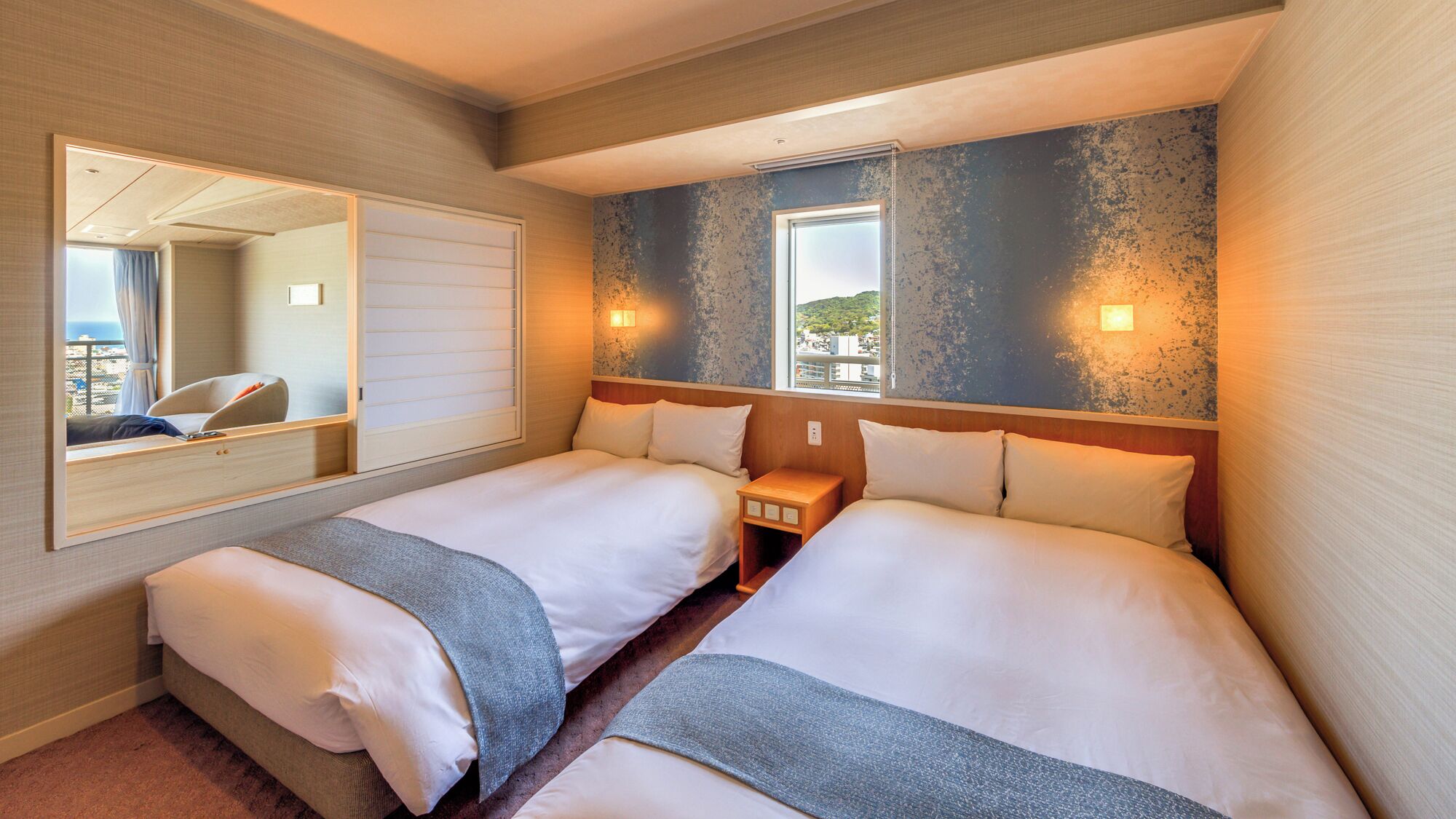 A hotel room with two beds, a large mirror, and a view of the city.