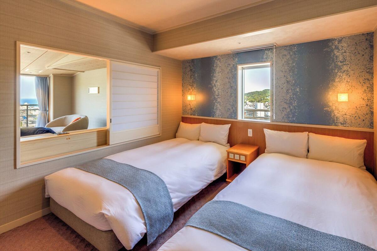 A hotel room with two beds, a large mirror, and a view of the city.