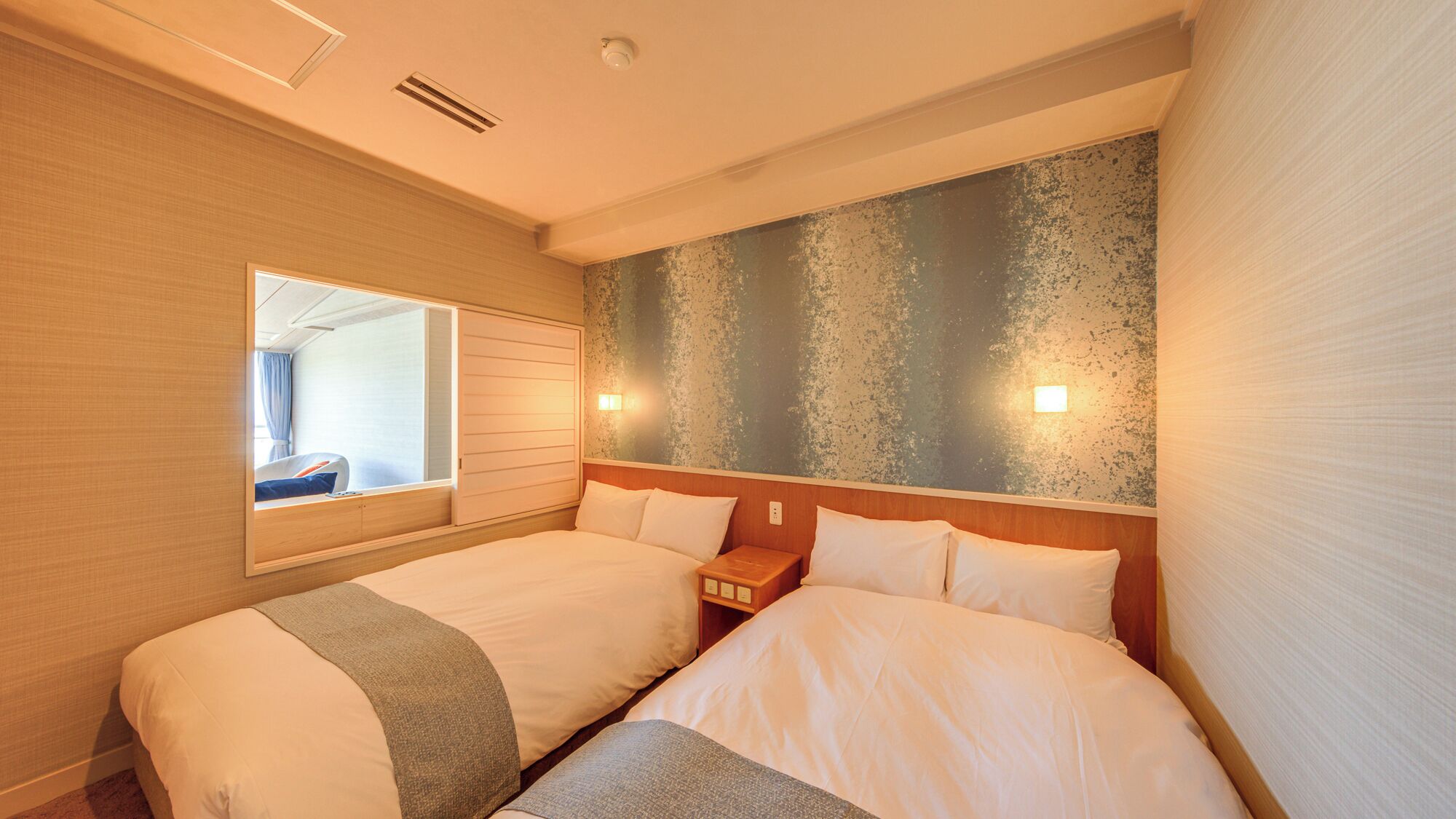 A hotel room with two beds, a large window, a textured wall, and a nightstand.