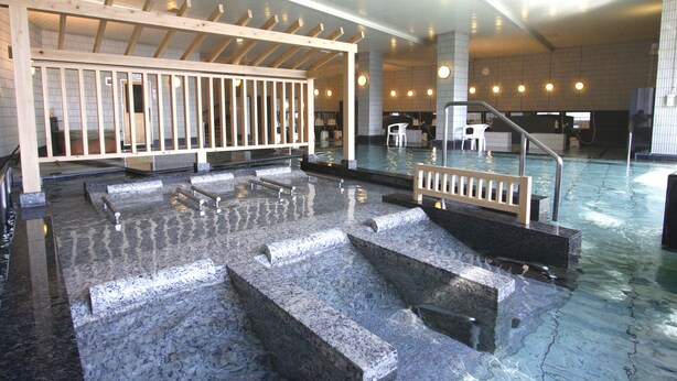 A public indoor swimming pool with multiple levels and steps, wooden railings, and a tiled floor. - Hotel Juraku (Ito)