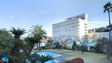 Un hotel con piscina rodeado de palmeras y un césped cuidado.
