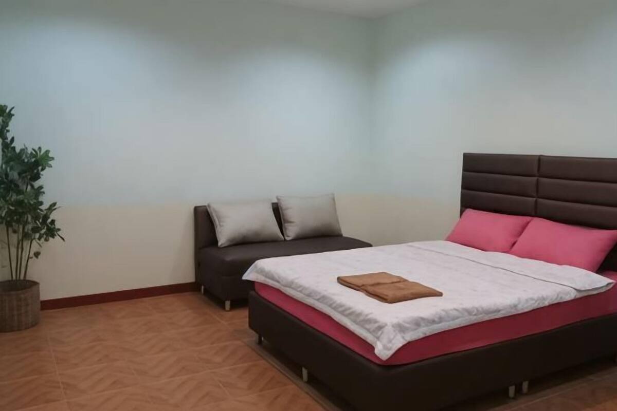 A bedroom with a bed, a sofa, and a potted plant.