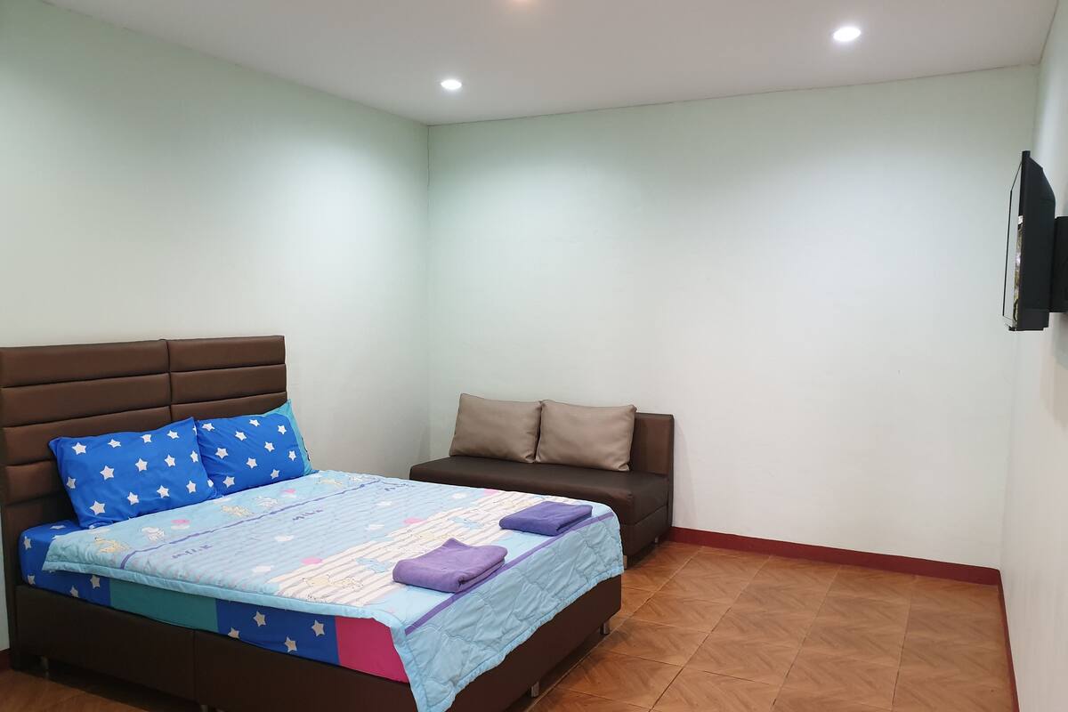 A bedroom with a bed, a sofa, and a TV mounted on the wall.