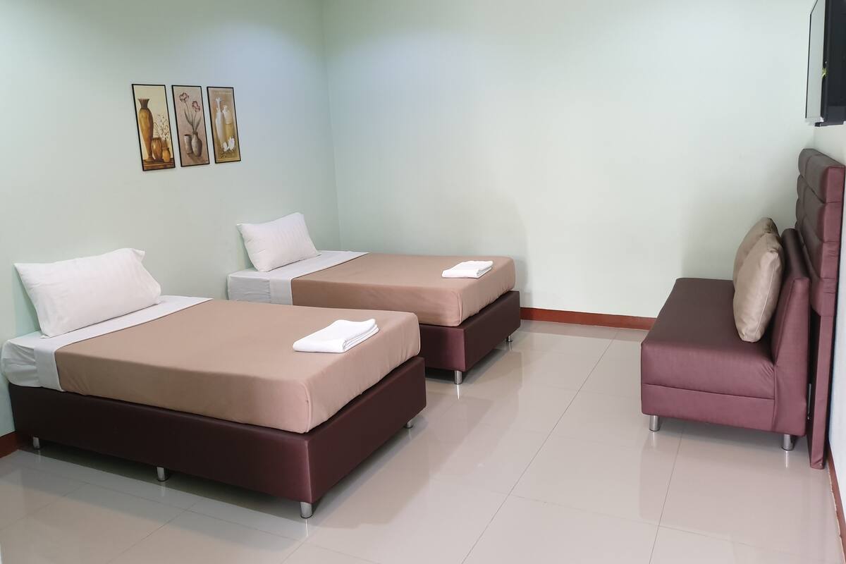 A hotel room with two beds, a sofa, and a flat-screen TV.