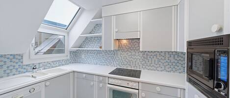 Una cocina compacta con tragaluz, armarios blancos, un microondas y un horno pequeño.