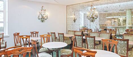 A dining area with multiple tables and chairs, a large mirror, and wall-mounted lighting fixtures.