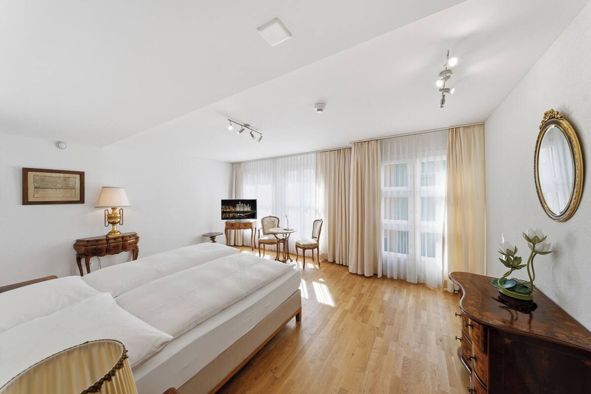 Quarto de hotel com cama, escrivaninha, cadeira, espelho e janela com cortinas.