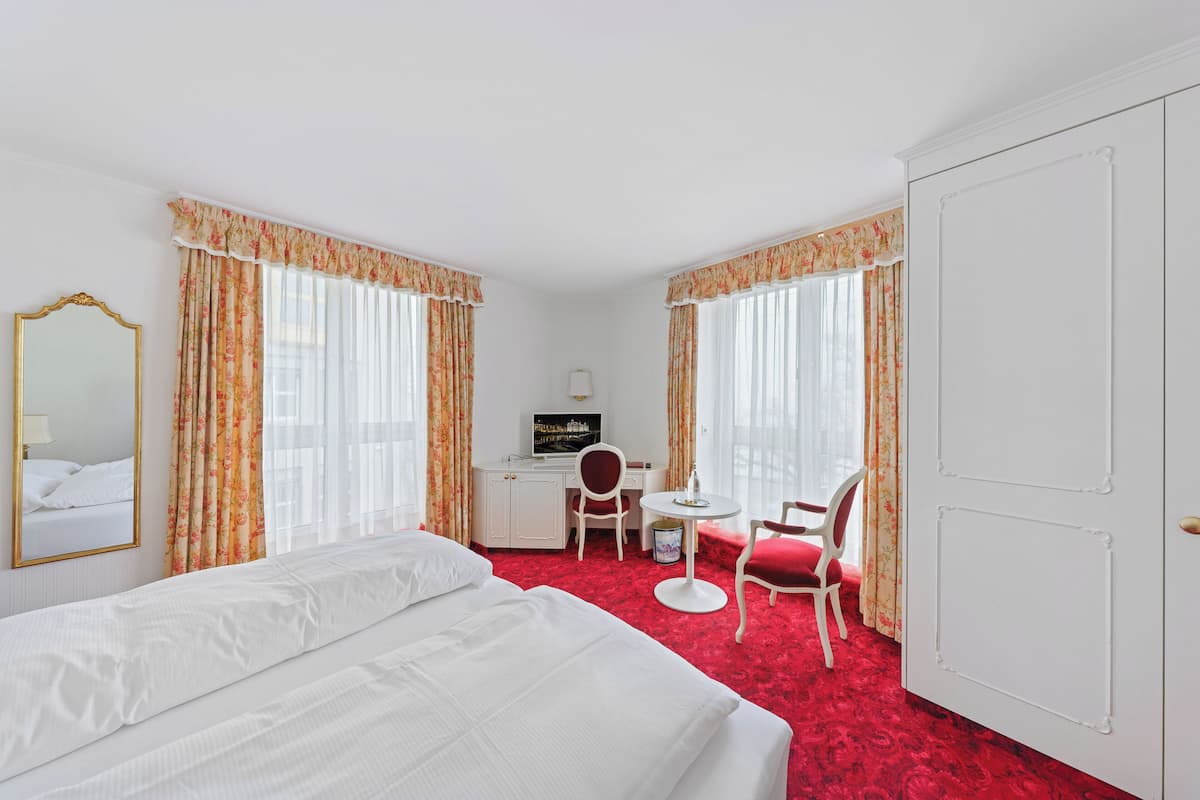 Quarto de hotel com uma cama, uma escrivaninha com cadeira, televisão e porta.