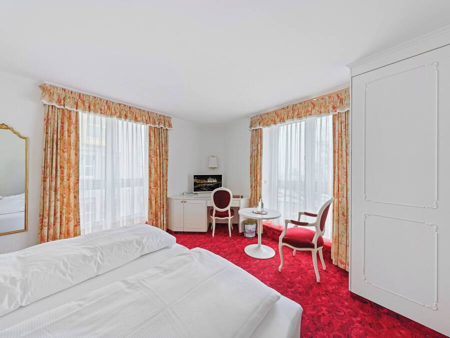Una habitación de hotel con una cama, un escritorio con silla, un televisor y una puerta.