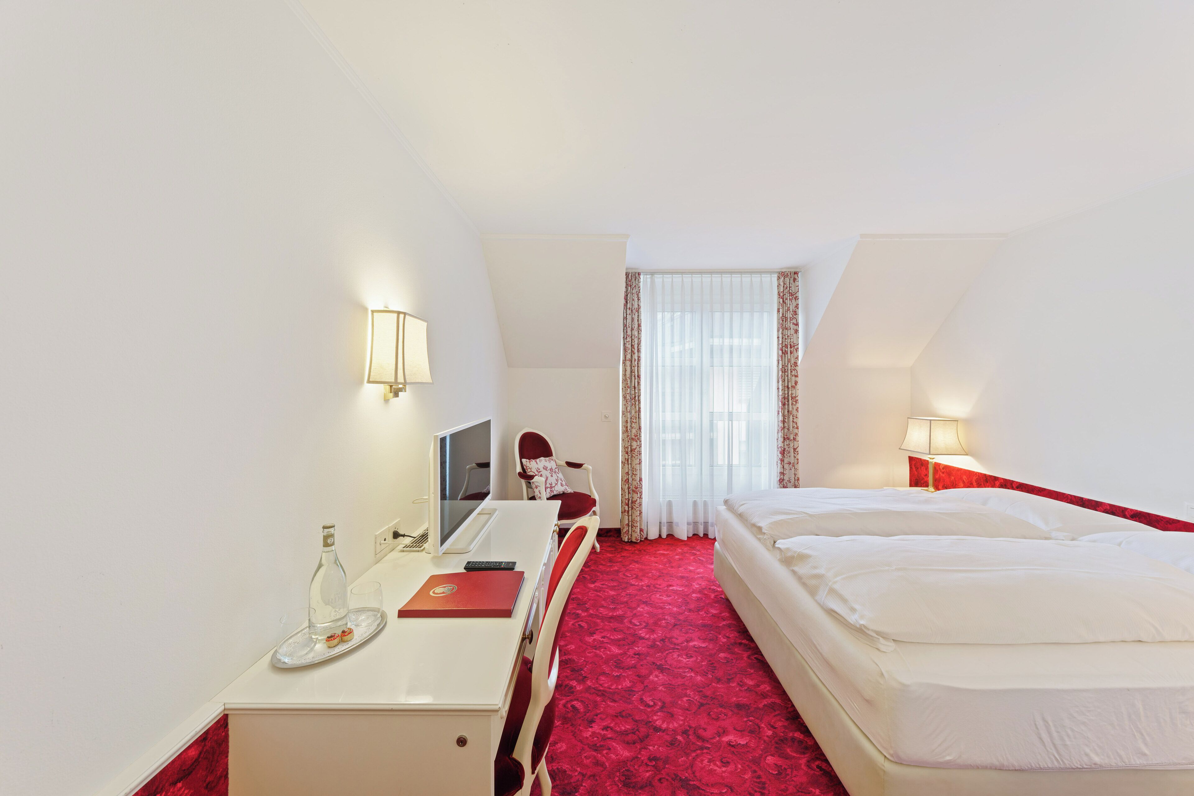 A hotel room with a desk, computer, chair, two beds, and a window with curtains.