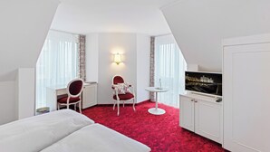 A hotel room with a bed, a desk, a chair, a television, and a red carpet. - Hotel Mozart Rorschach (Rorschach)