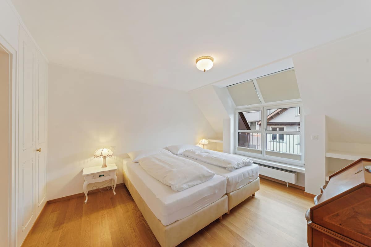 Quarto com cama, abajures, janela e radiador.