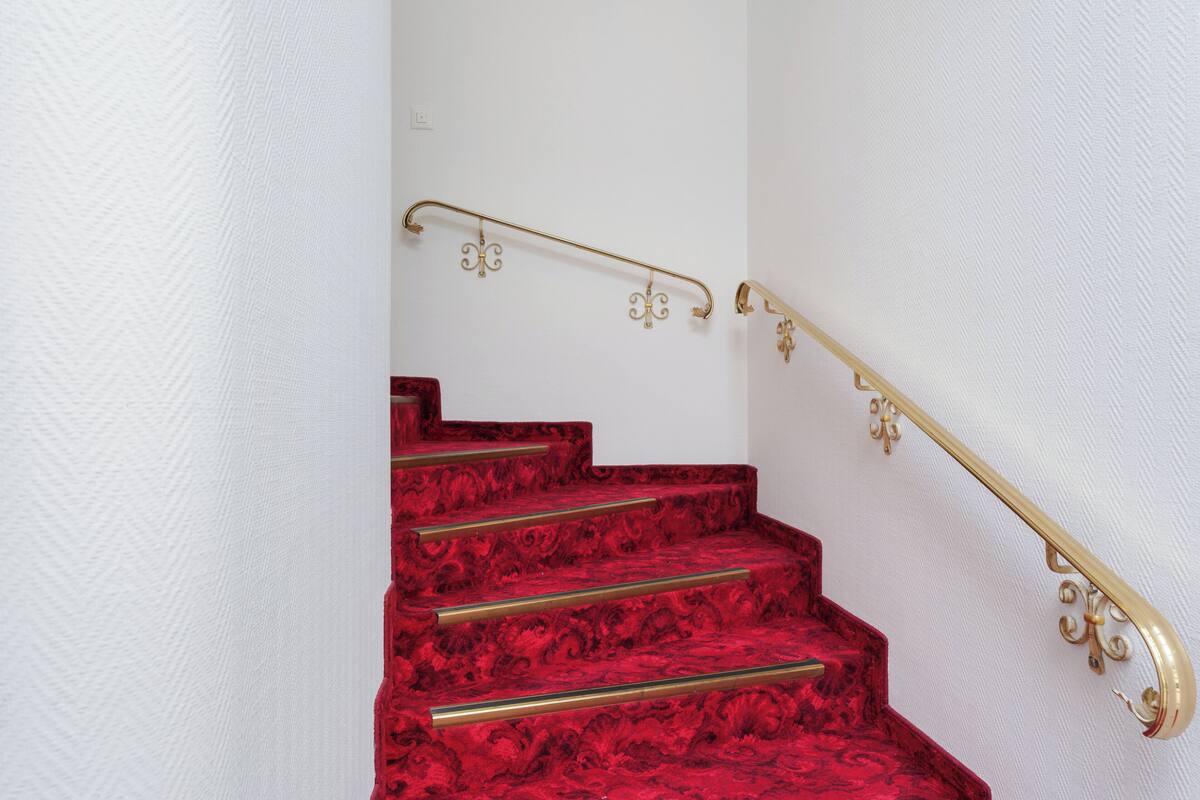 Escadaria com tapete vermelho e corrimãos dourados.
