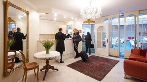 A hotel lobby with a large mirror, a round table with a vase, a red sofa, and a chandelier. - Hotel Mozart Rorschach (Rorschach)