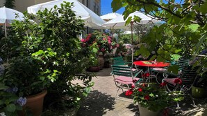 An outdoor patio area with green metal chairs and tables, surrounded by potted plants and flowers. - Hotel Mozart Rorschach (Rorschach)