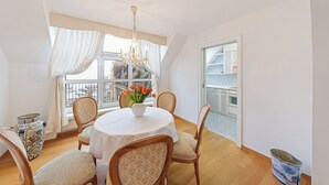 A dining area with a round table, chairs, a vase with flowers, a chandelier, and a view of the balcony. - Hotel Mozart Rorschach (Rorschach)