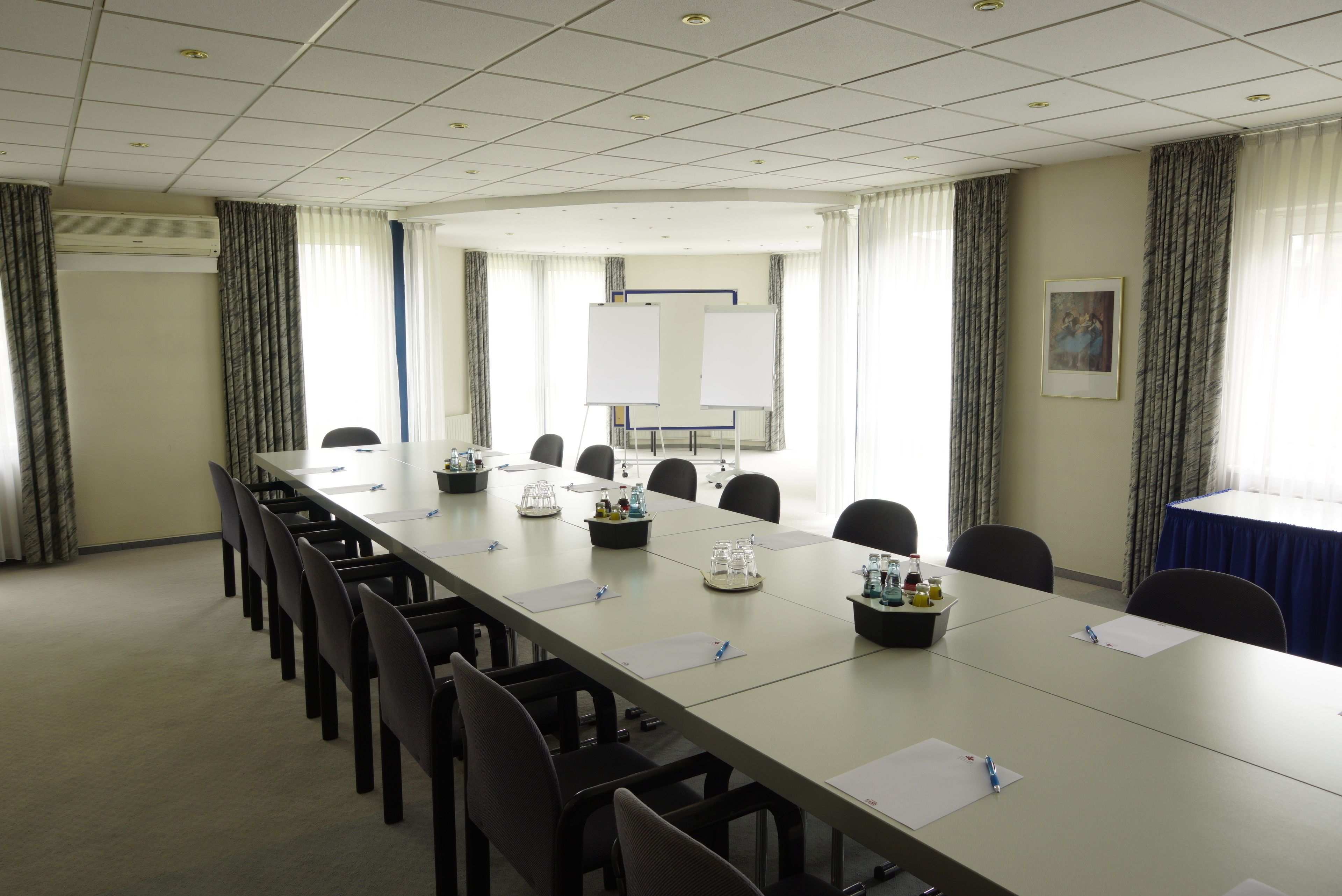 Un salón de conferencias con una larga mesa, sillas, una pizarra y una pantalla para proyector.
