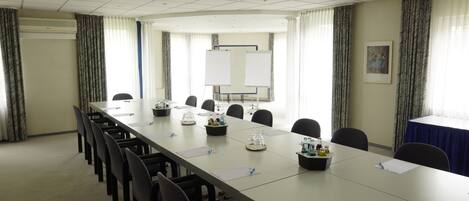 Un salón de conferencias con una larga mesa, sillas, una pizarra y una pantalla para proyector.