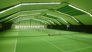 An indoor tennis court with green flooring and a high ceiling with linear lighting. - Trans World Hotel Auefeld (Hann. Muenden)
