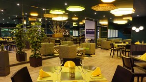 A restaurant with multiple dining tables, chairs, and potted plants. - Trans World Hotel Auefeld (Hann. Muenden)