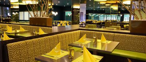 Ein Restaurant mit Sitzgelegenheiten in Form von Boxen und Tischen, an jedem Tisch gelbe Servietten und Besteck.