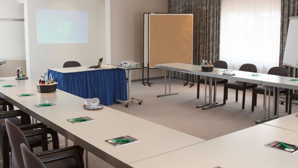 A conference room with a long table, chairs, a projector screen, and a whiteboard. - Trans World Hotel Auefeld (Hann. Muenden)