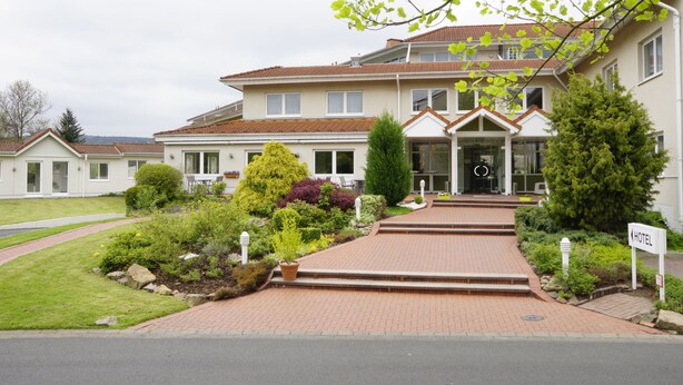 A hotel with a brick entrance, a well-maintained garden, and a clear view of the building's entrance. - Trans World Hotel Auefeld (Hann. Muenden)