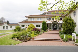A hotel with a brick entrance, a well-maintained garden, and a clear view of the building's entrance. - Trans World Hotel Auefeld (Hann. Muenden)