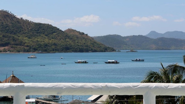 A coastal view with boats on the water, a white structure in the foreground, and hills in the background. - GMG Hotel (Coron)