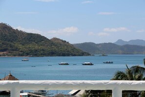 A coastal view with boats on the water, a white structure in the foreground, and hills in the background. - GMG Hotel (Coron)
