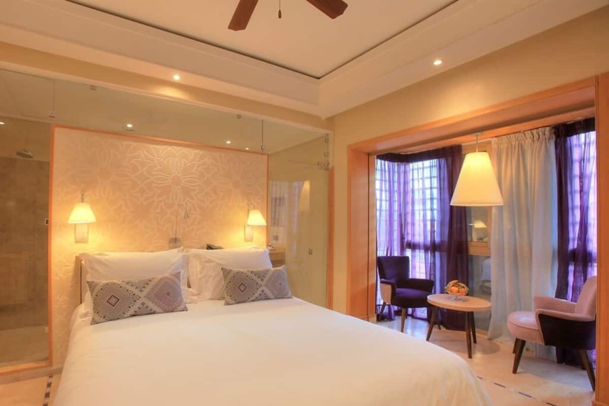 A hotel room with a large bed, two chairs, a small table, and a mirror.