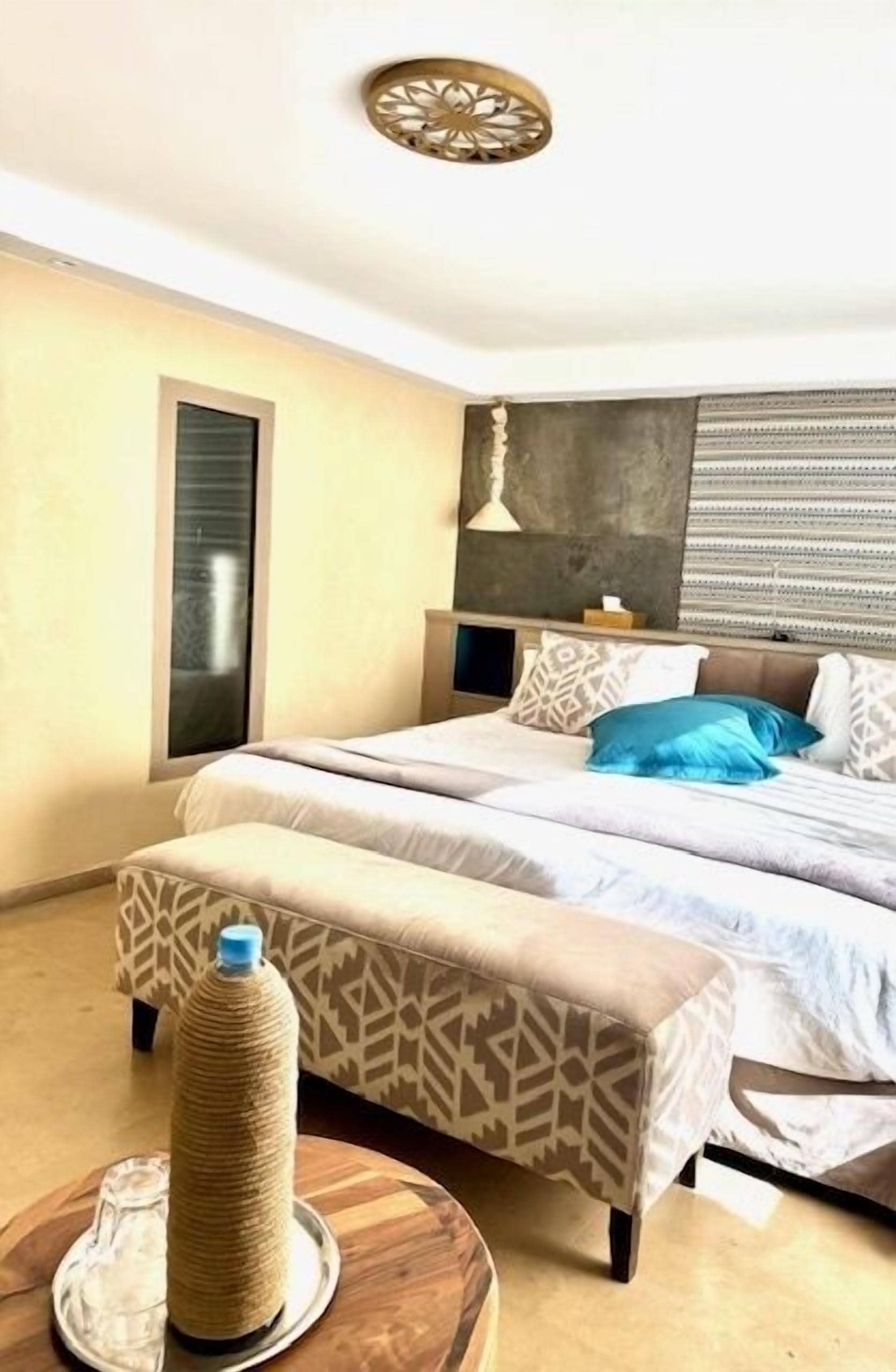 A bedroom with a bed, a bedside table, a lamp, a window, and a cat tree.