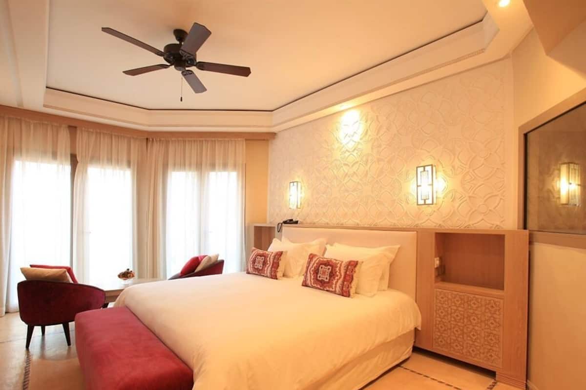 A hotel room with a large bed, a ceiling fan, a red armchair, and a decorative wall.