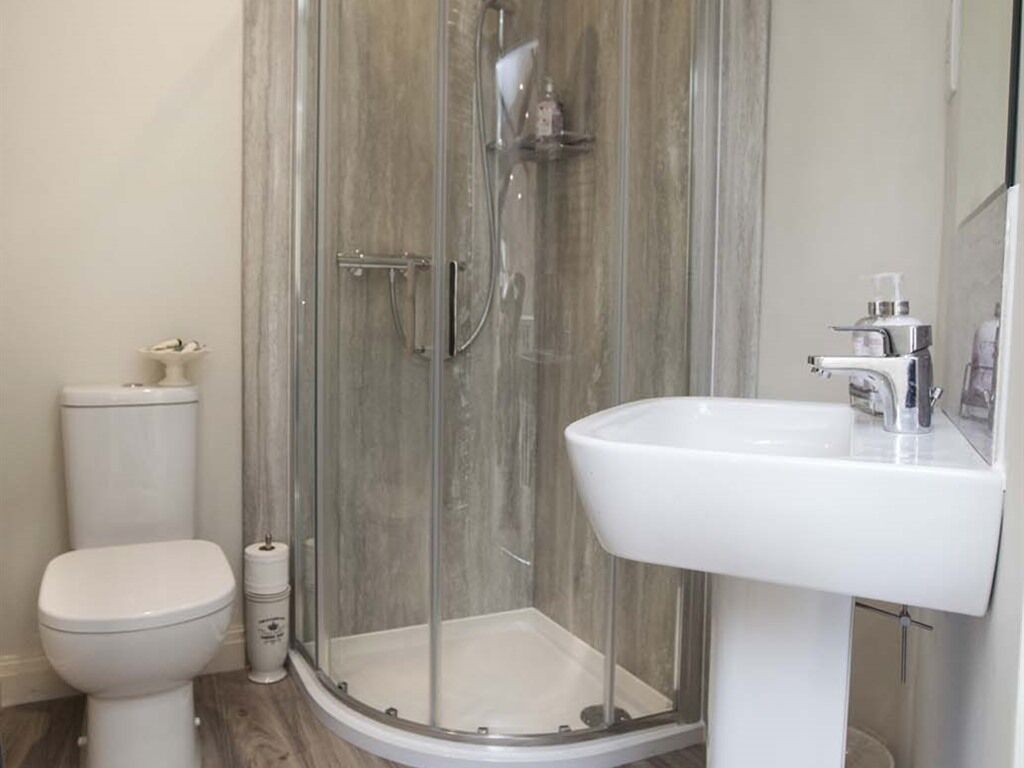 Un baño con ducha de vidrio, lavamanos blanco y retrete.