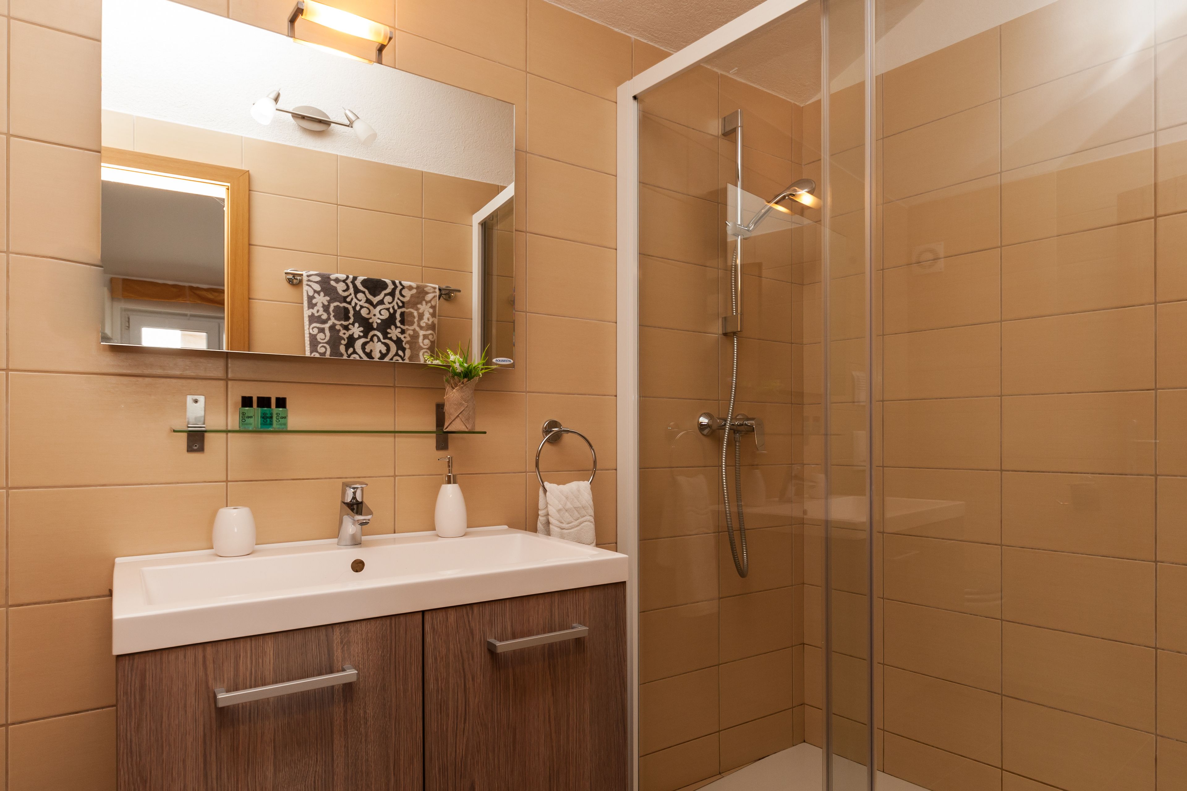 Un bagno moderno con cabina doccia in vetro, un lavandino bianco con specchio sopra e un mobile bagno in legno.