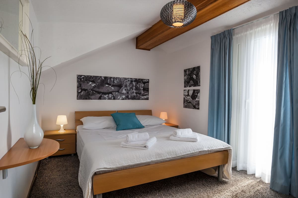 A modern bedroom with a wooden bed, white bedding, a teal pillow, and two wall-mounted artworks.