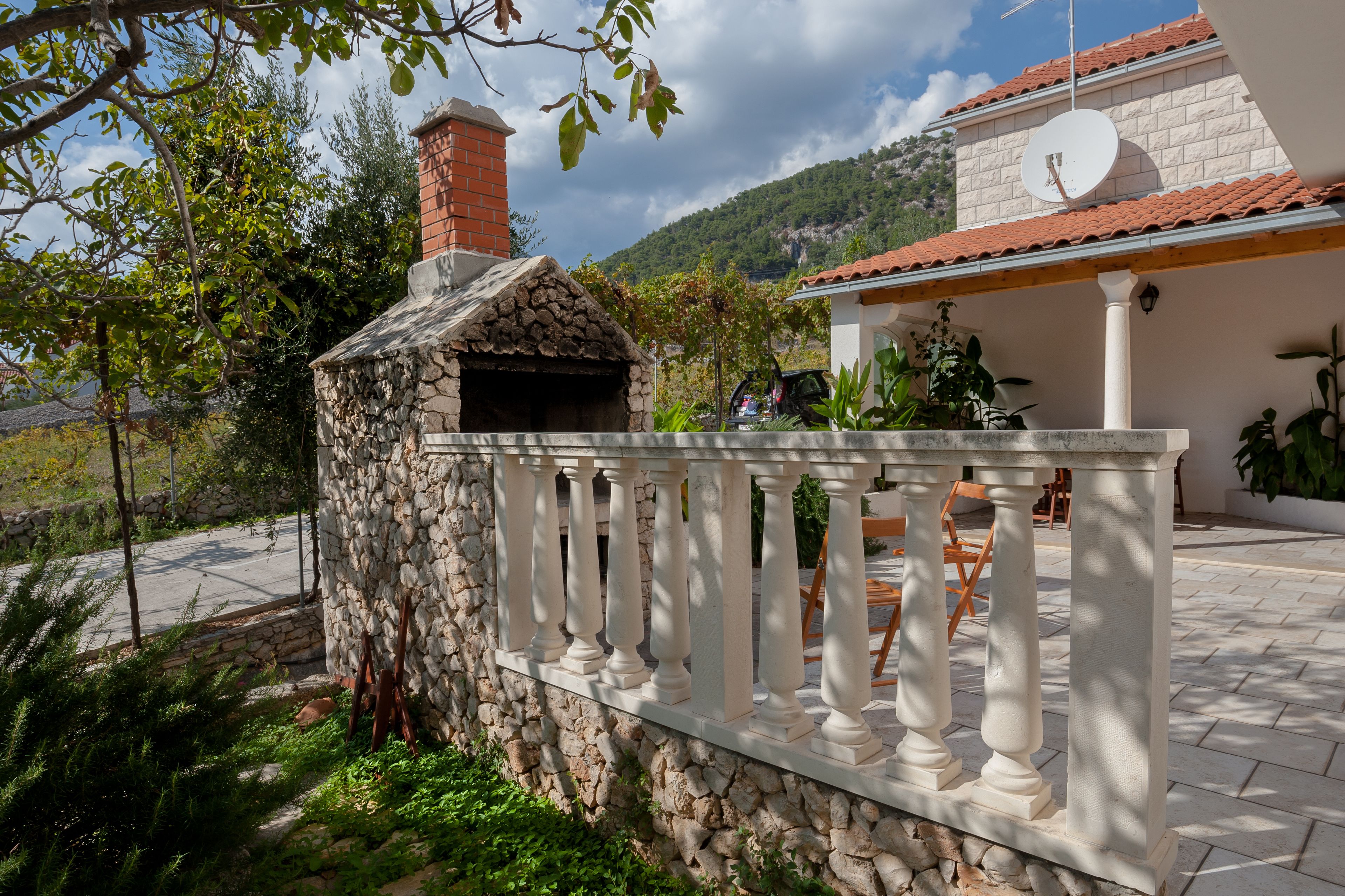 A stone building with a brick chimney, a white balcony with balusters, and a satellite dish on the roof.