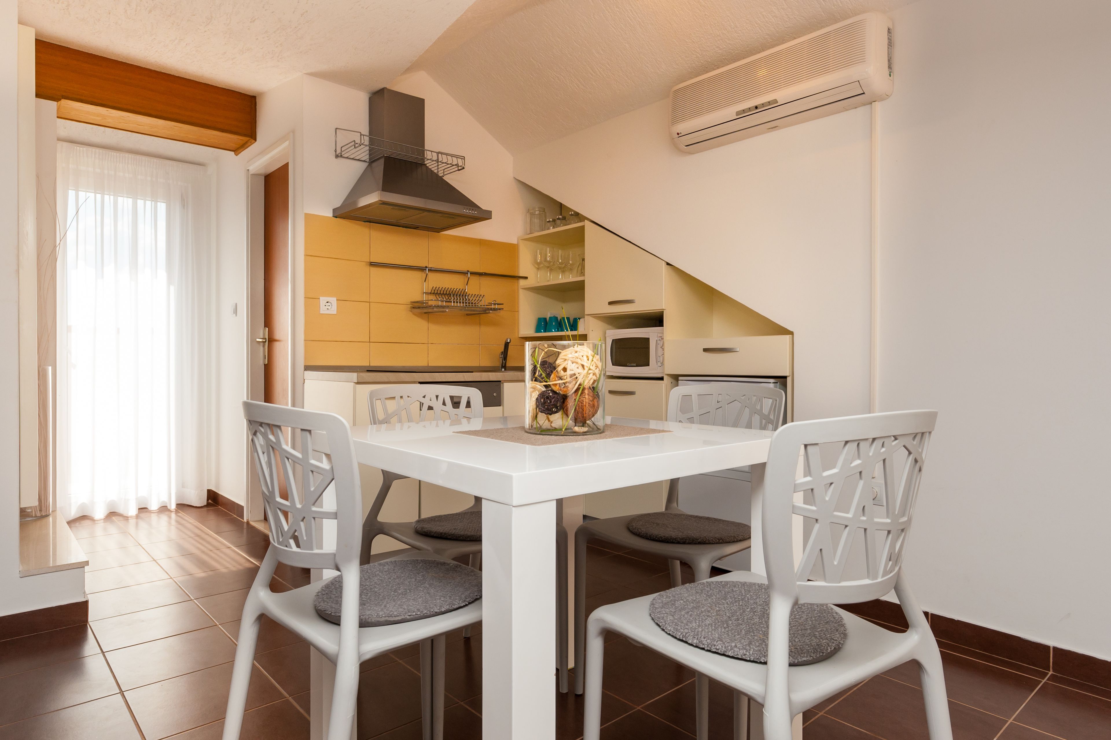 A compact kitchen with white cabinets, a microwave, and a built-in oven. There is a dining table with four chairs and a decorative vase.