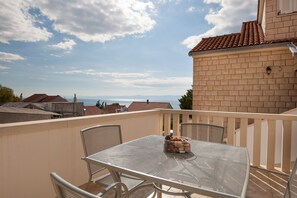 Un balcon avec une table et des chaises, une vue sur la mer et un bâtiment en briques.