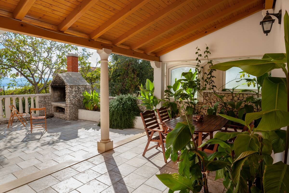 A covered patio with stone flooring, wooden furniture, and a stone-built fireplace.