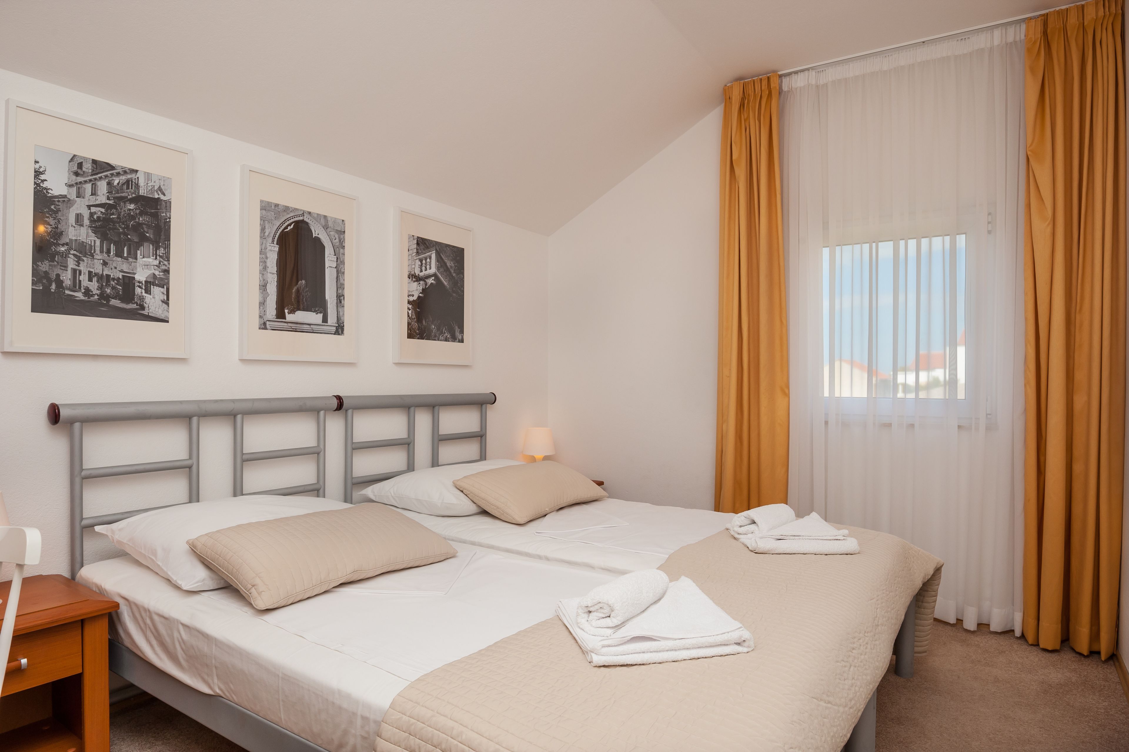 Een hotelkamer met twee bedden, een nachtkastje, een lamp en drie ingelijste foto’s aan de muur.