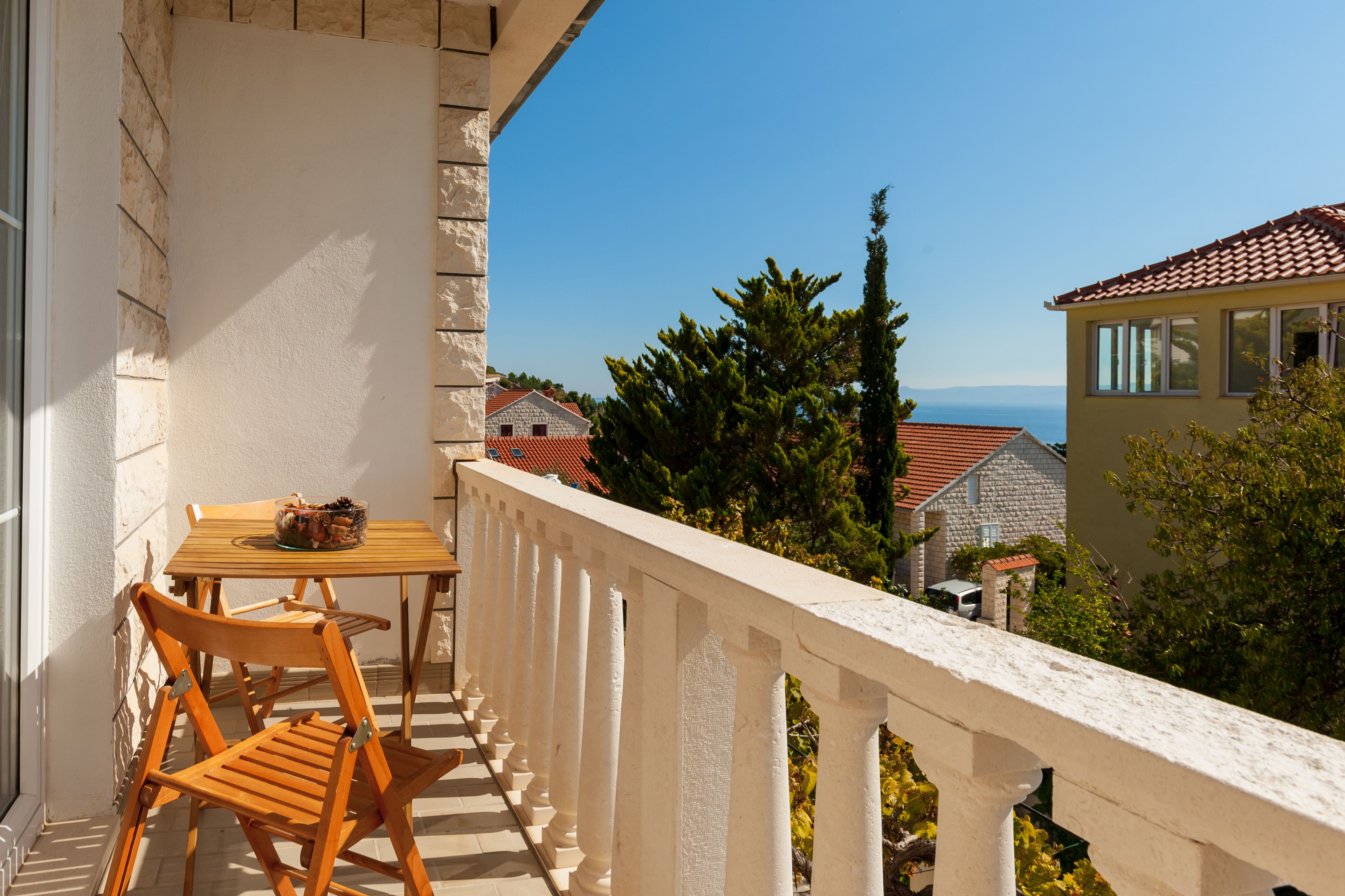 A balcony with a table and chairs, overlooking a coastal area with houses and trees.