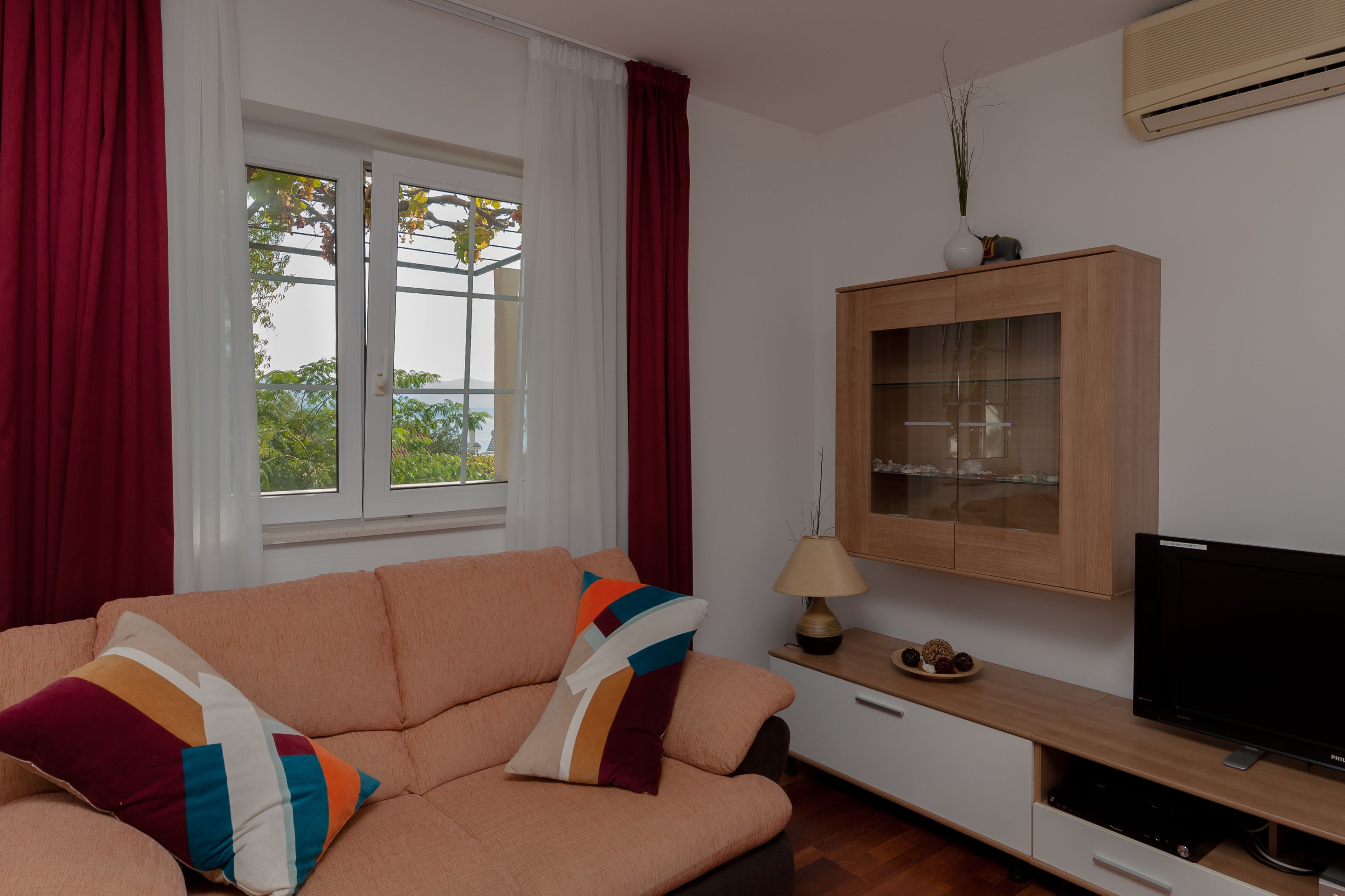 Een woonkamer met een bank, een televisie, een kast en een raam met gordijnen.