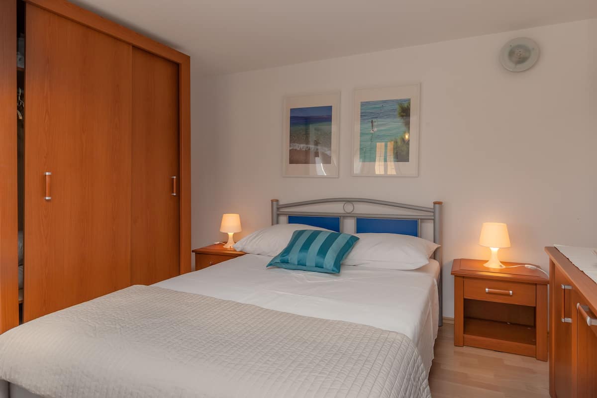 A bedroom with a large bed, two bedside tables with lamps, a wooden wardrobe, and two framed pictures on the wall.